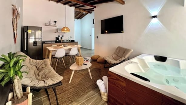 Un salon chaleureux avec un jacuzzi, une table à manger, des chaises et une cuisine en arrière-plan.
