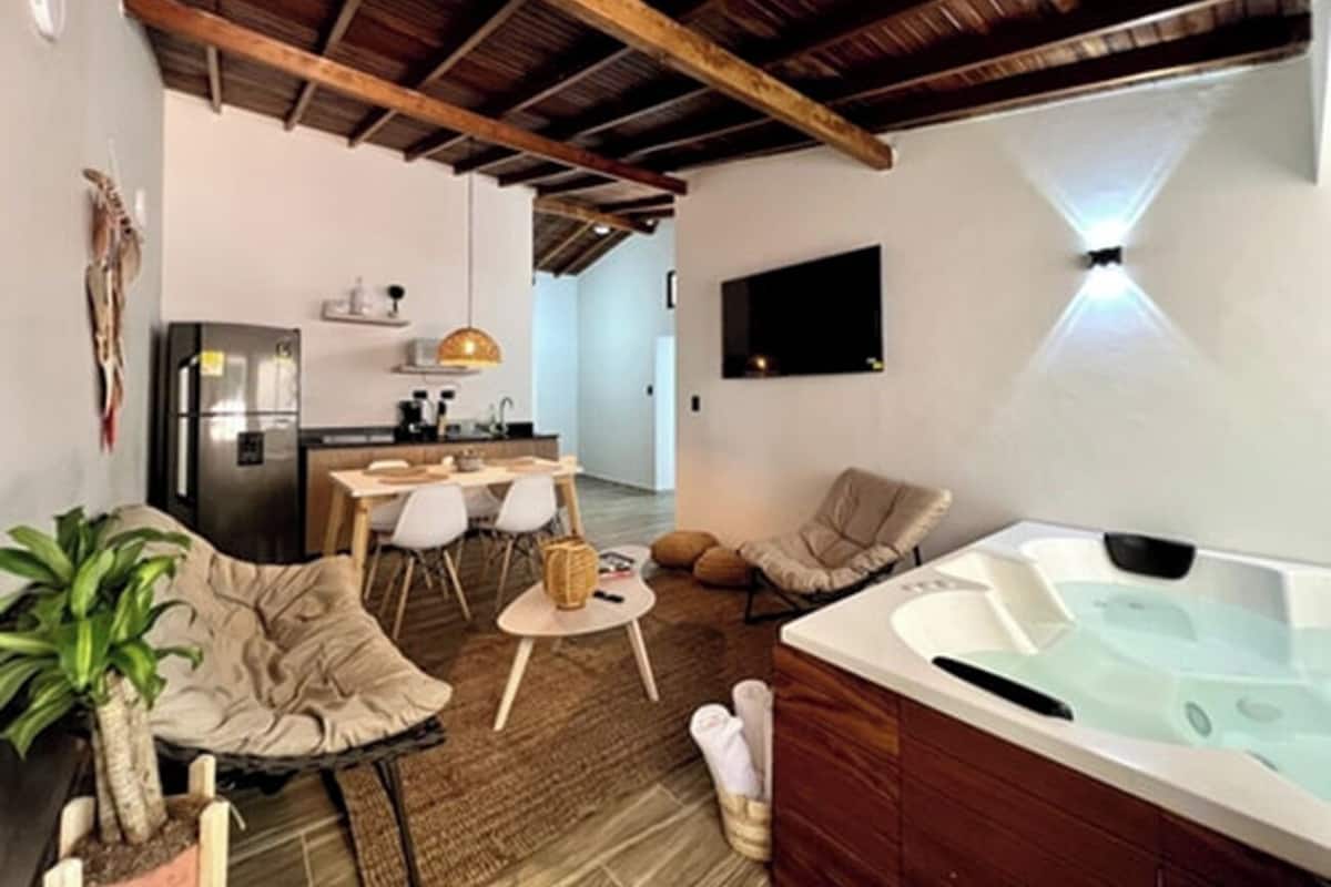Uma sala de estar aconchegante com hidromassagem, uma mesa de jantar, cadeiras e uma cozinha ao fundo.