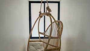 Un fauteuil suspendu en osier, doté d’un coussin, placé devant une fenêtre à cadre noir.