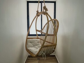 A wicker hanging chair with a cushion, positioned in front of a window with a black frame. - Cumbiana Loft in Provenza by Nowa (Medellín)