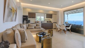 Una sala de estar moderna con sofá, mesa de centro y sillas, una cocina con armarios y electrodomésticos, y un ventanal con vistas.