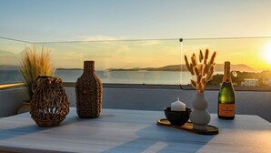 Un balcón con jarrones de mimbre, una vela, una botella de Veuve Clicquot y vista al mar al atardecer.