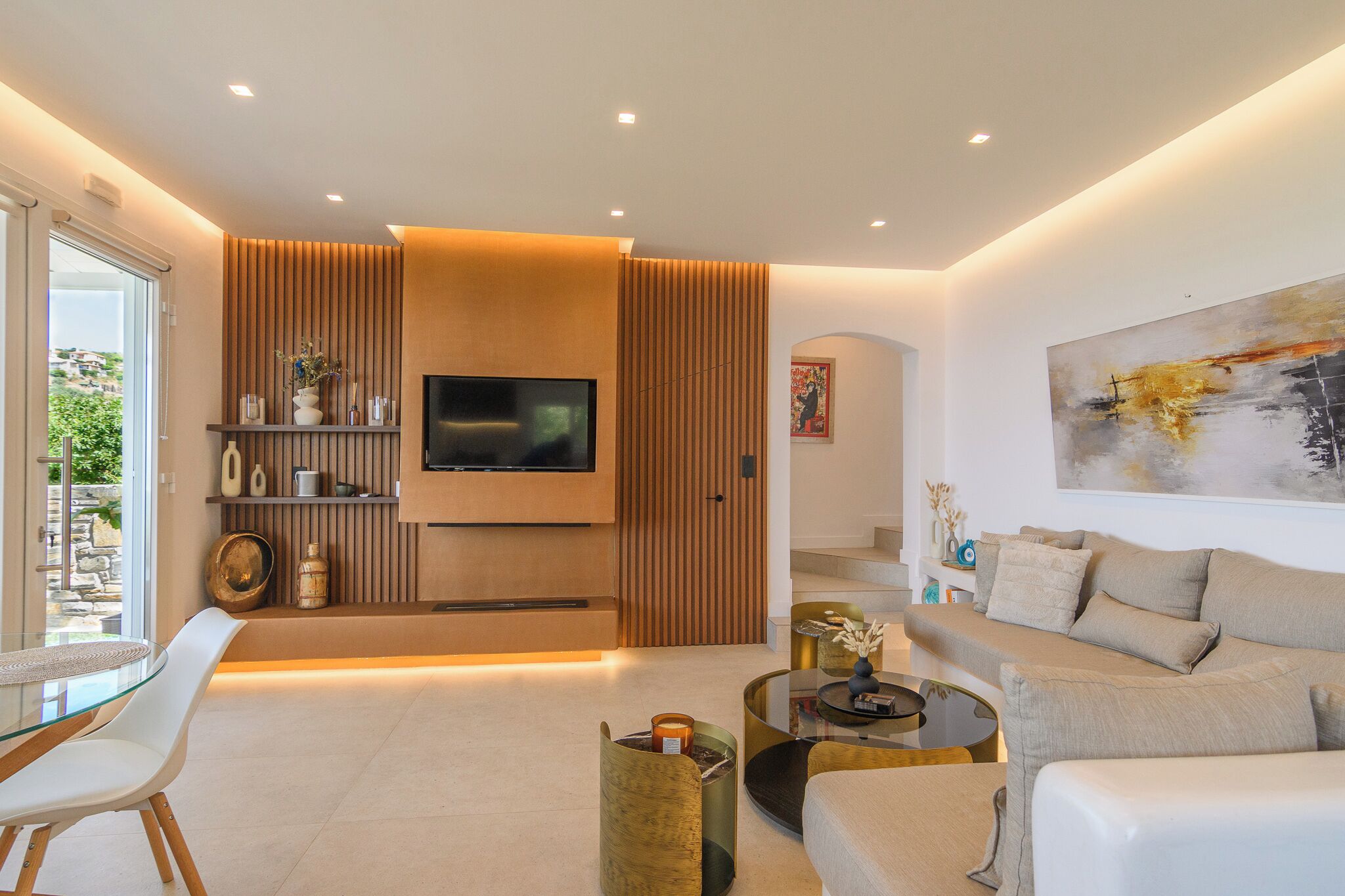 A modern living room with a flat-screen TV, a sofa, a coffee table, and a dining area with a glass table and chairs.