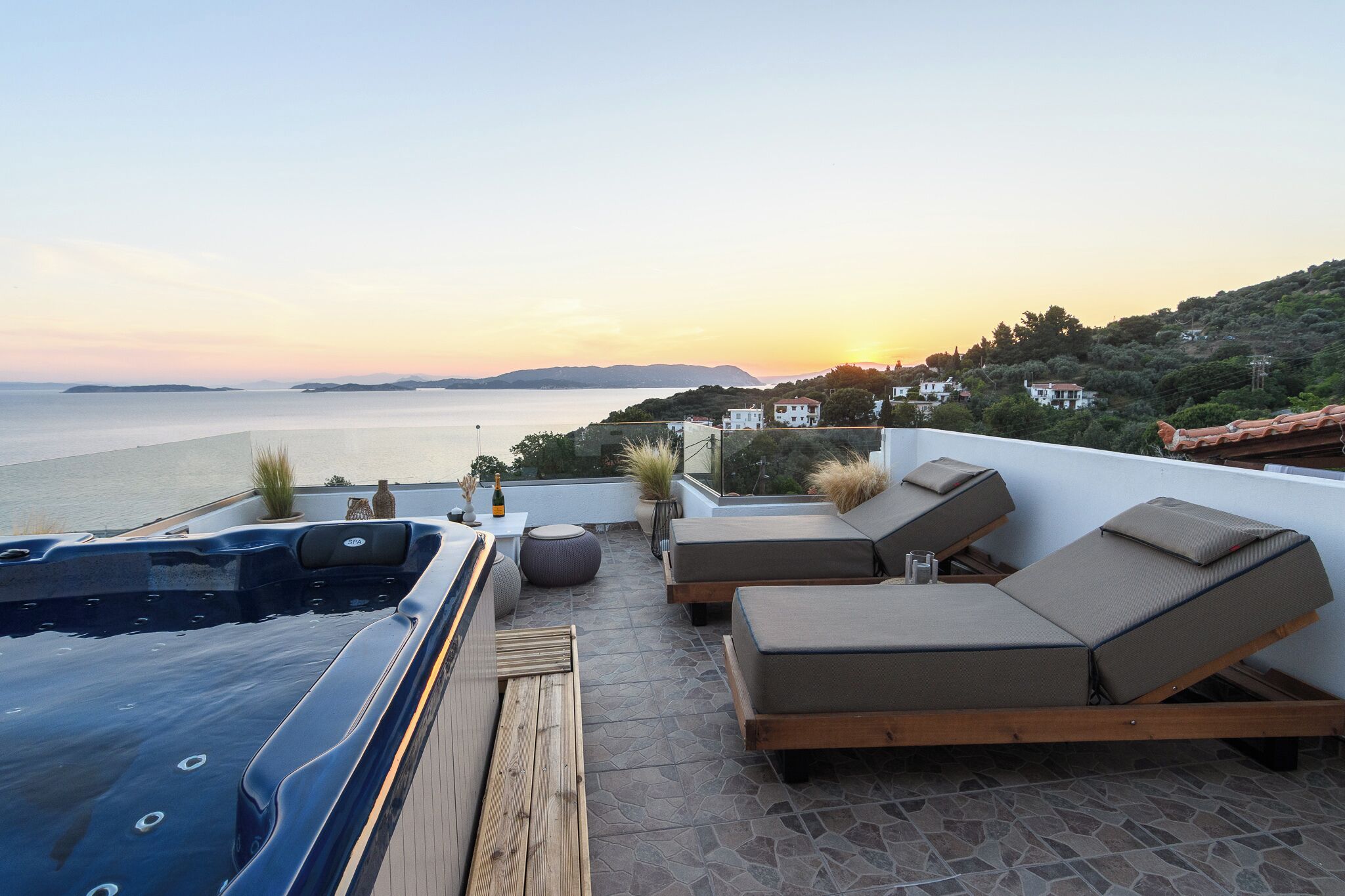 Una terraza en la azotea con un jacuzzi, sillones de descanso y vistas al mar al atardecer.