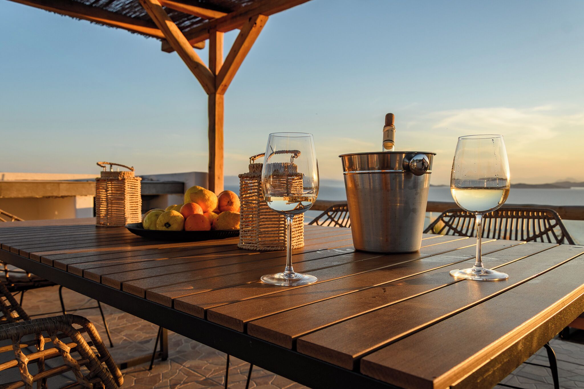 A wooden table with two wine glasses, a metal bucket, and wicker baskets containing fruits.
