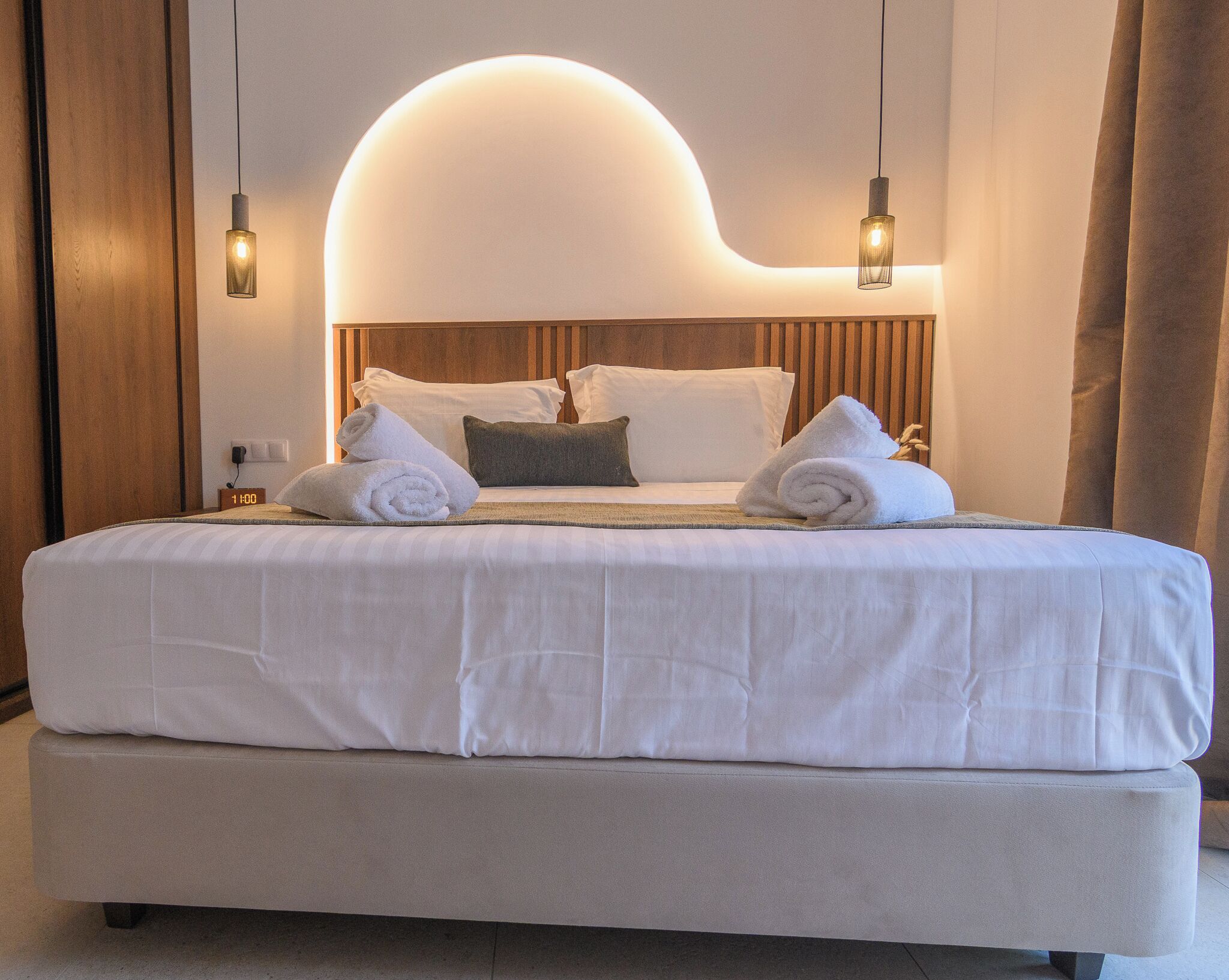 Una habitación de hotel moderna con una cama grande, un cabecero de madera y dos lámparas colgantes.