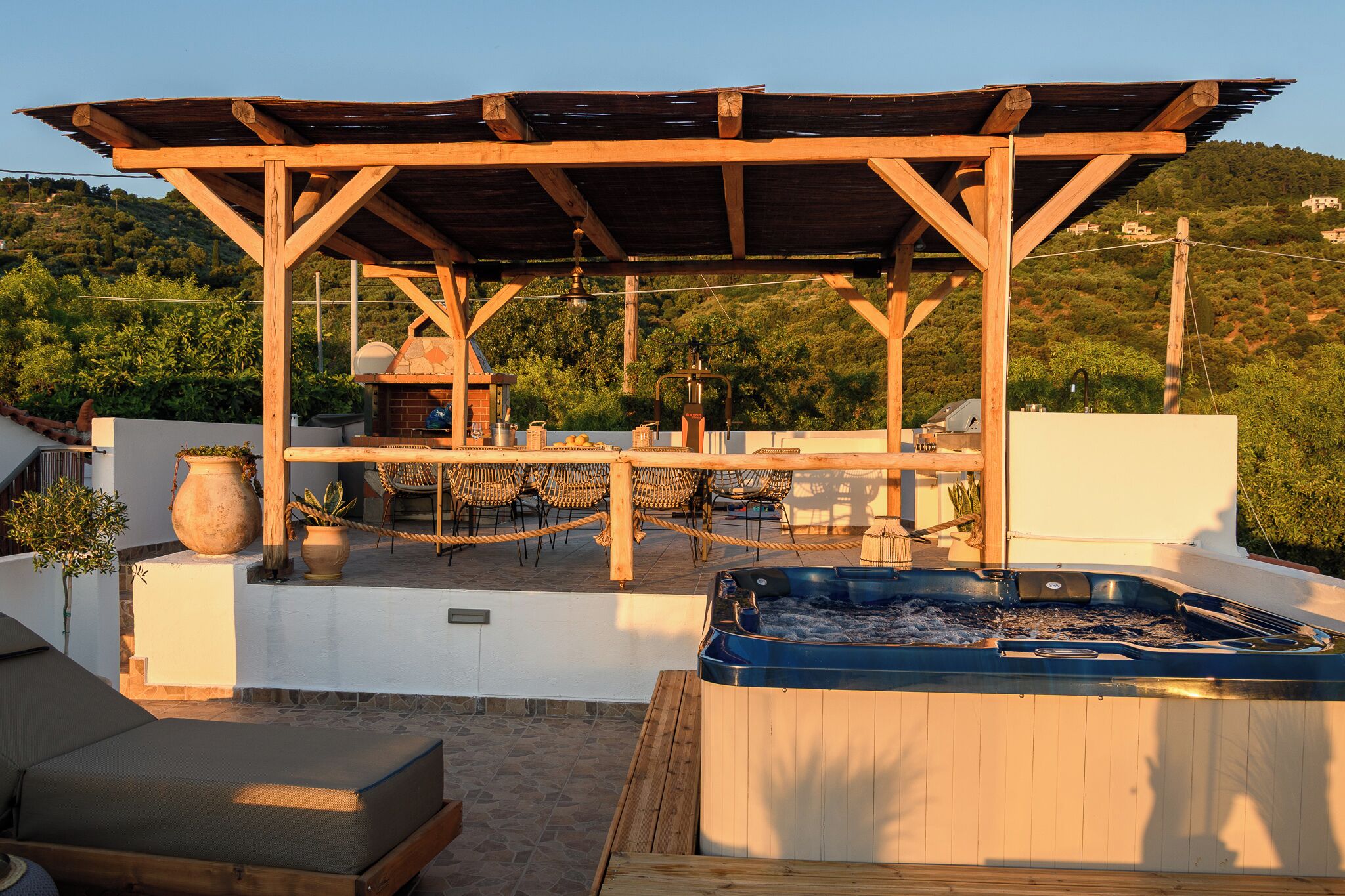 A wooden pergola with a barbecue, outdoor seating, and a hot tub on a rooftop terrace.