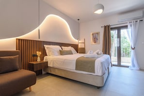 Una habitación de hotel moderna con una cama grande, un sofá, una mesita de noche y vistas al exterior.
