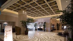Un hall espacioso con piso estampado, una columna grande y plantas en macetas.