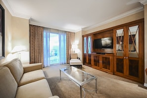 Ein Hotelzimmer mit einer Couch, einem Sessel, einem Fernseher und einem Glastisch.