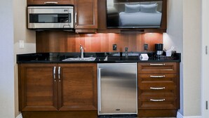 A compact kitchen with a built-in microwave, a stainless steel refrigerator, and wooden cabinetry.
