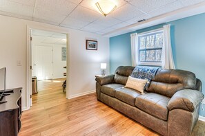 A living room with a brown leather sofa, a lamp, a window with curtains, and a door leading to another room. - Tranquil 1-bedroom apartment with AC in charming Toccoa (Toccoa)