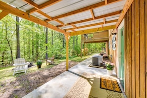 A covered porch with a wooden deck, a white Adirondack chair, a potted plant, and a welcome mat.