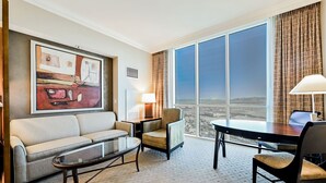 Ein Hotelzimmer mit großem Fenster, einer Couch, einem Sessel, einem kleinen Tisch und einer Lampe.