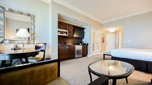A hotel room with a bed, a round glass table, a sofa, a kitchenette, and a large mirror. - SVS: PH Floor Studio | Signature at MGM (Las Vegas)