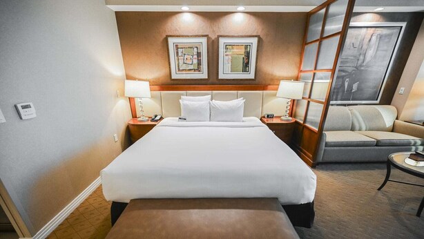 A hotel room with a large bed, a sofa, a small table, and two bedside lamps. - SVS: Strip View Studio | Signature at MGM (Las Vegas)