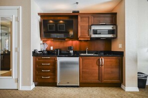 A compact kitchen with wooden cabinets, a stainless steel refrigerator, a microwave, and a dishwasher. - SVS: Strip View Balcony | Signature at MGM (Las Vegas)