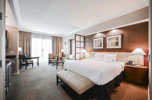 Ein Hotelzimmer mit einem großen Bett, einem Schreibtisch, einem Stuhl, einem kleinen Tisch und einem Nachttisch mit einer Lampe.