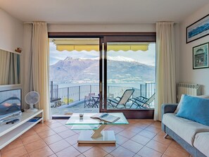Una sala de estar con televisor, una mesa de centro de vidrio, un sofá y un balcón con vistas a la montaña.