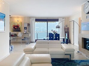 Ein modernes Wohnzimmer mit einer Couch, einem Essbereich mit Stühlen, einem Tisch, einem Kamin und Blick ins Freie.