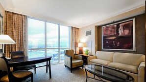 A hotel room with a large window, a desk with a chair, a sofa, a coffee table, and a lamp. - SVS: Strip View Studio | Signature at MGM (Las Vegas)