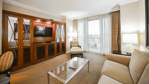 Ein Hotelzimmer mit Fernseher, einer Couch, einem Sessel, einem Glastisch und Blick auf die Stadt.