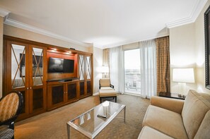 Ein Hotelzimmer mit Fernseher, einer Couch, einem Sessel, einem Glastisch und Blick auf die Stadt.