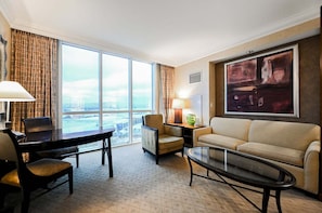 Ein Hotelzimmer mit großem Fenster, Schreibtisch, Sofa, Couchtisch und einem Gemälde an der Wand.