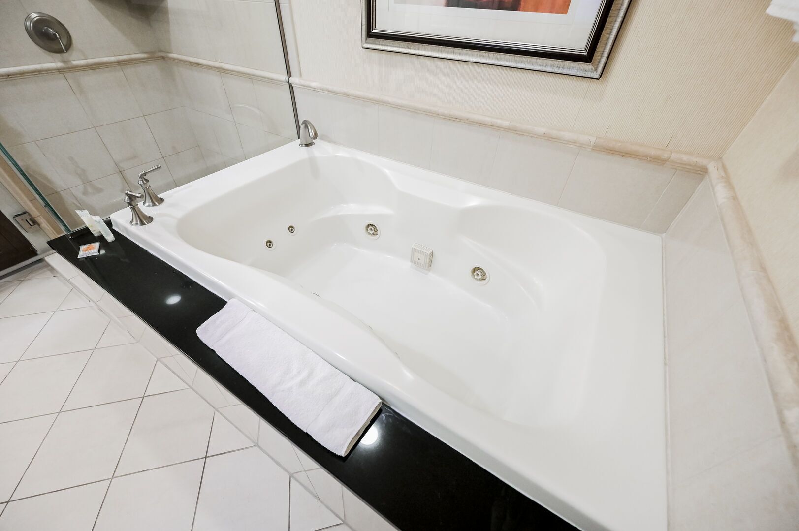 A modern bathroom with a large white bathtub, a black countertop, and a framed picture on the wall.