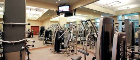 Un gimnasio con diferentes máquinas de ejercicio, un televisor montado en el techo y un espejo en la pared.