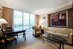A hotel room with a large window, a desk with a chair, a sofa, a coffee table, and a lamp. - SVS: PH Floor Studio | Signature at MGM (Las Vegas)
