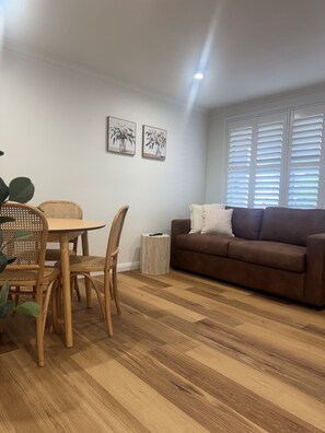 A living room with a brown sofa, a dining table with chairs, and two framed pictures on the wall.
