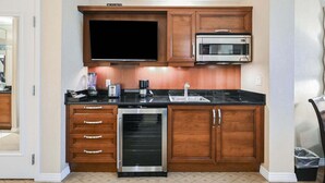 A kitchen with wooden cabinets, a microwave, a dishwasher, and a large flat-screen TV. - SVS: PH Floor Strip View Balcony | Signature at MGM (Las Vegas)