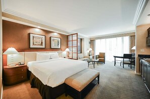 Ein Hotelzimmer mit einem großen Bett, Nachttischen, einem Schreibtisch, einem Sessel und Blick ins Freie.
