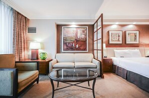 A hotel room with a bed, a sofa, a glass coffee table, a lamp, and a painting on the wall. - Studio • No Resort Fee • Free Parking A3B1 (Las Vegas)