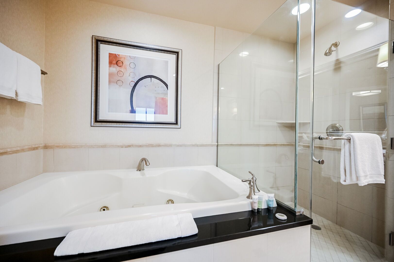 A modern bathroom with a large bathtub, a glass shower enclosure, and a framed artwork on the wall.