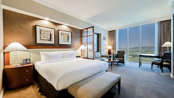 A hotel room with a large bed, two bedside tables with lamps, a desk with a chair, and a large window offering a view.