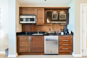 A kitchen with wooden cabinets, a stainless steel dishwasher, and a microwave. - SVS: Sphere Strip View Studio | Signature at MGM (Las Vegas)