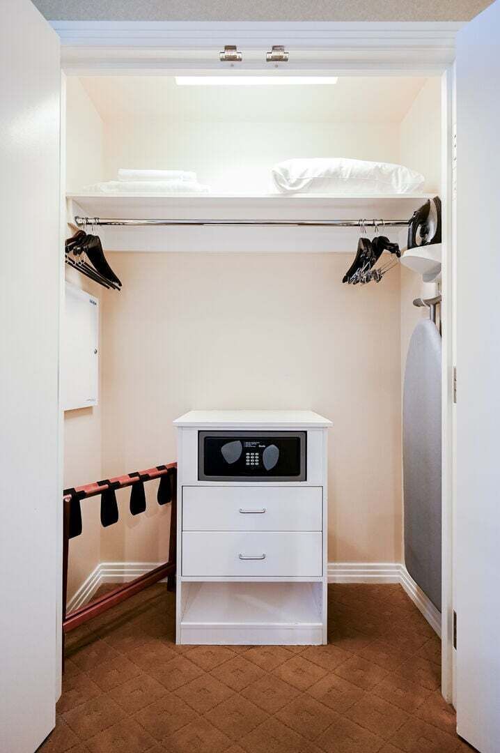 Une chambre à coucher de taille modeste, avec un lit superposé, une petite commode blanche et un placard où sont suspendus les vêtements.