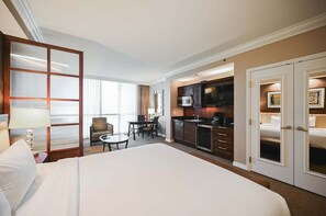 A hotel room with a large bed, a dining table with chairs, a kitchenette, and a separate seating area with a view. - SVS: Strip View Studio | Signature at MGM (Las Vegas)