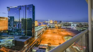 Ett högt hotell med en modern fasad av glas, en parkeringsplats och utsikt över stadsbilden i skymningen.