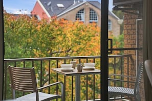 A balcony with a table, chairs, and a view of trees and buildings.