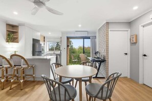A modern kitchen with white cabinets, a dining area with a round table and chairs, and a balcony with a view.