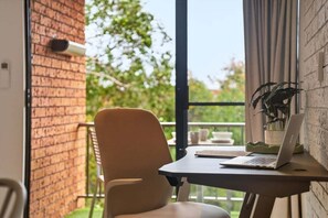 A room with a brick wall, a window, a chair, a table with a laptop, and a potted plant.