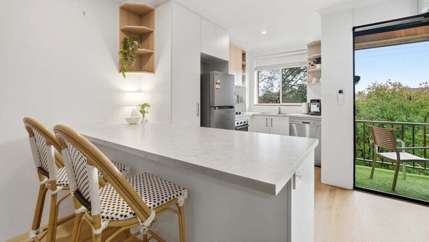 Una cocina moderna con armarios blancos, una isla central y un comedor con sillas de mimbre.