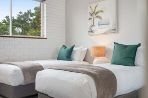A room with two beds, a window, a lamp, and a painting on the wall.