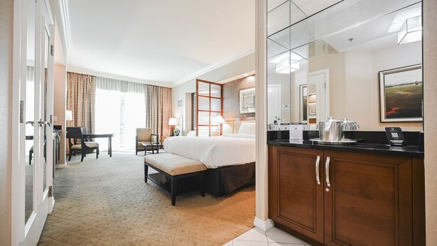 A hotel room with a bed, a desk, a chair, a sofa, a dining table, and a kitchen area with a coffee maker. - SVS: PH Floor Strip View Balcony | Signature at MGM (Las Vegas)