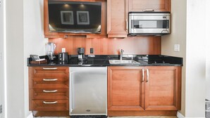 A compact kitchen with wooden cabinets, a built-in microwave, a dishwasher, and a coffee maker. - SVS: PH Floor Strip View Balcony | Signature at MGM (Las Vegas)
