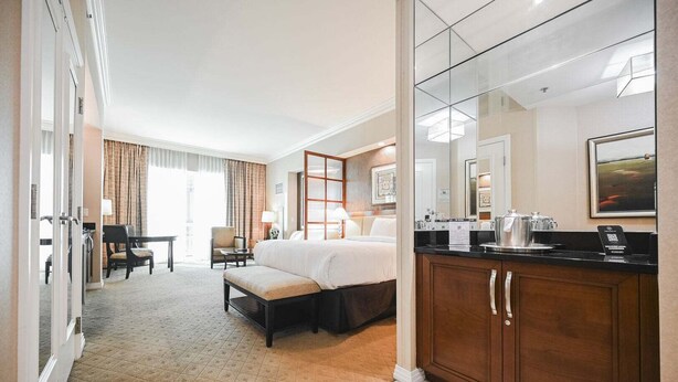 Ein Hotelzimmer mit Bett, Schreibtisch, Stuhl, Sofa, Badezimmer mit Spiegel und einer Kaffeemaschine.