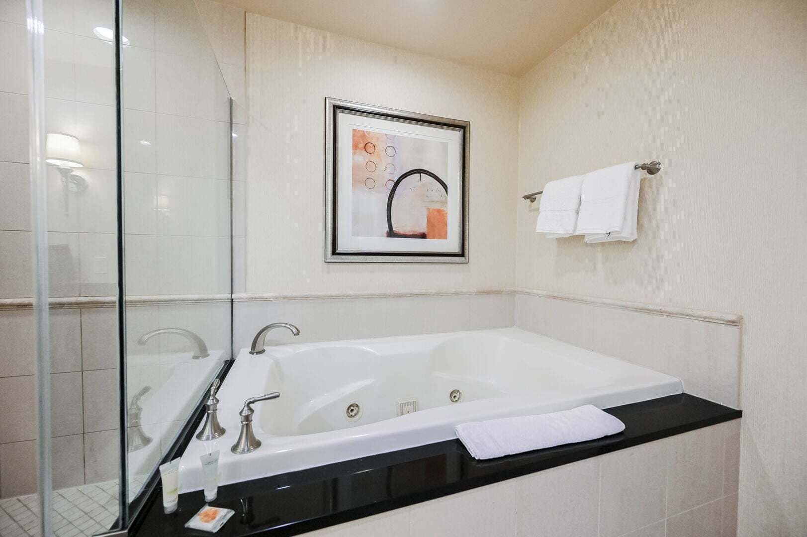 Ein modernes Badezimmer mit einer großen Badewanne, einer Duschkabine aus Glas und einem gerahmten Kunstwerk an der Wand.